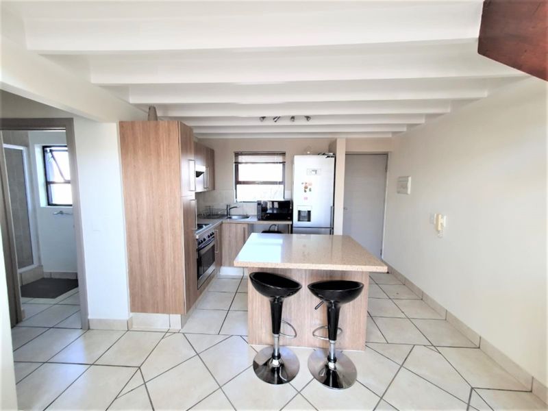 Modern kitchen featuring a central island with stone countertops, built-in oven, hob, and tiled flooring under an exposed beam ceiling.