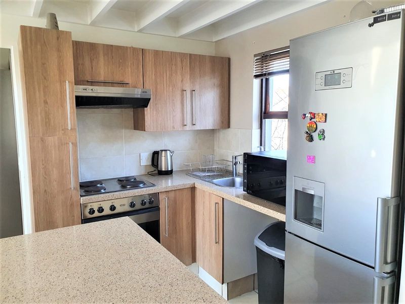 A functional kitchen featuring wood-look cabinetry, stone-look countertops, an electric hob with extractor fan, and a stainless steel sink with a tiled backsplash.