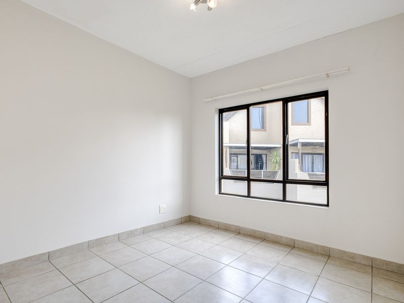 A bright, empty bedroom featuring neutral tiled flooring, a built-in cupboard, and large aluminium-framed windows providing natural light.