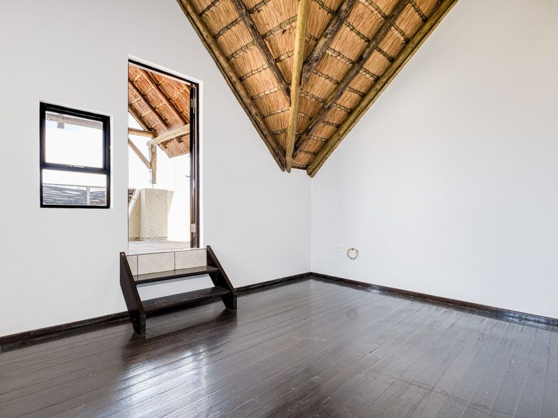 Empty bedroom featuring exposed thatch roof rafters, dark timber flooring, and direct access to an outdoor balcony area.