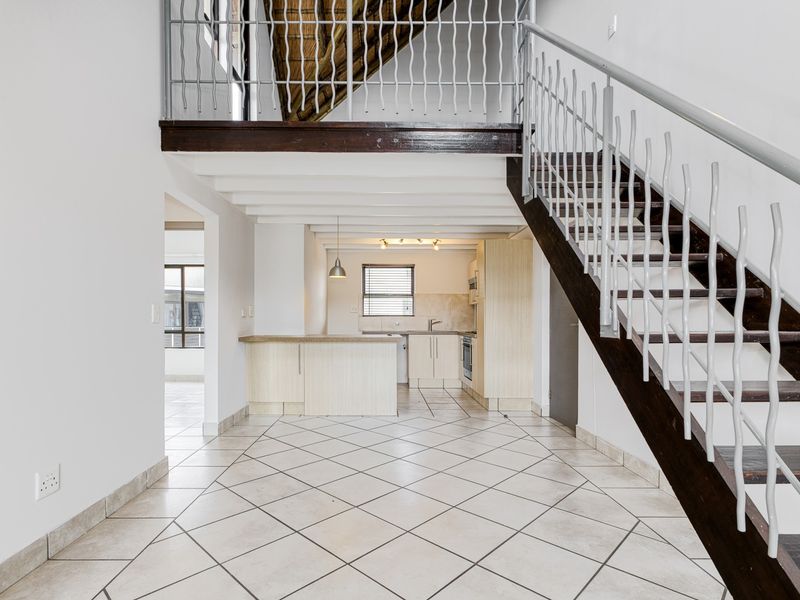 Open plan living area featuring a kitchen with built-in cabinetry, tiled flooring, and a staircase leading to an upper level.