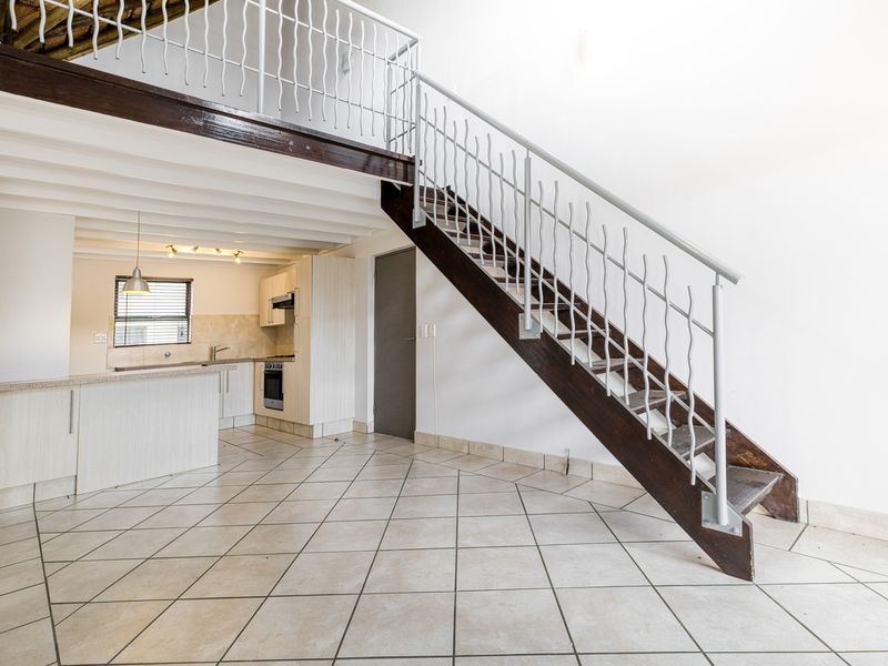 Open-plan living area featuring a mezzanine level, staircase with metal balustrade, tiled flooring, and a functional kitchen with built-in appliances.