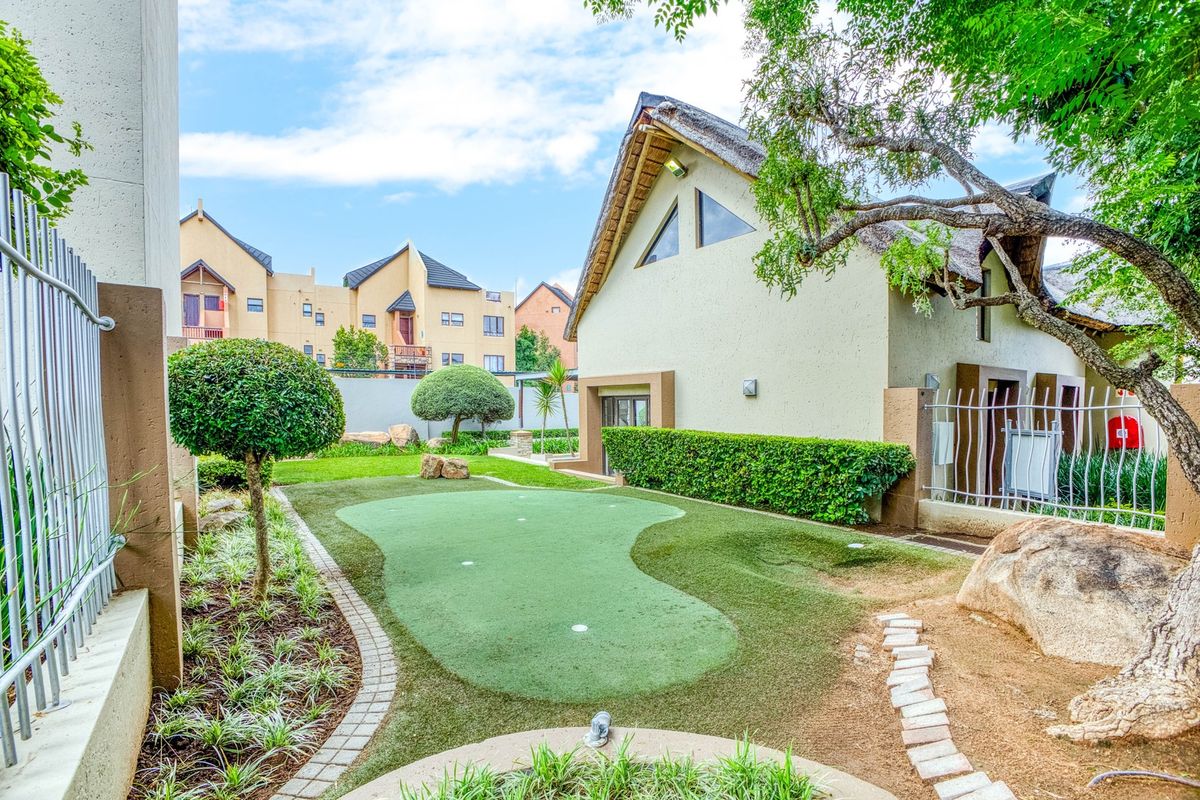 A well-maintained rear garden area featuring a private putting green, manicured landscaping, and a distinctive building with a thatched roof.