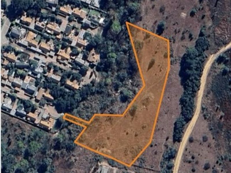Aerial view of a vacant residential plot with boundary lines highlighted, showing surrounding vegetation and proximity to established residential housing.