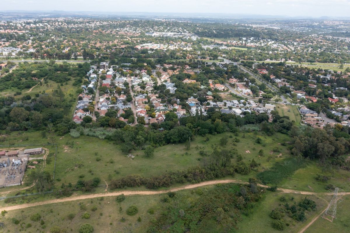 Aerial view of a vacant residential land parcel adjacent to an established suburban neighborhood with mature trees and infrastructure.
