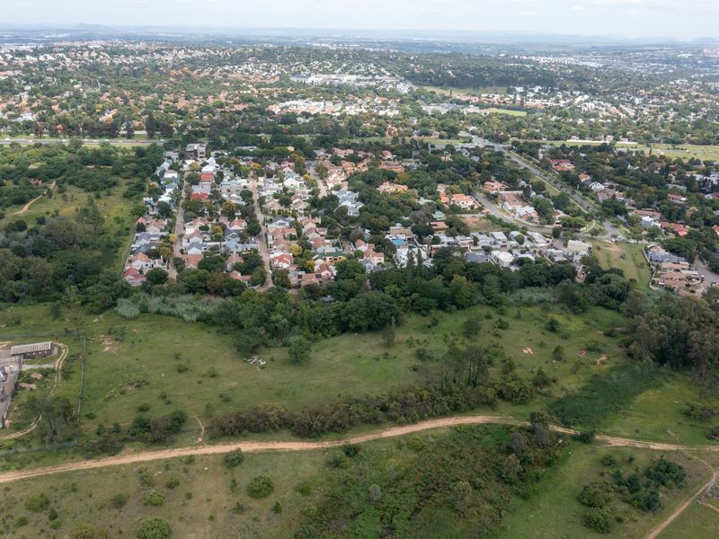 Aerial view of a vacant residential land parcel adjacent to an established suburban neighborhood with mature trees and infrastructure.