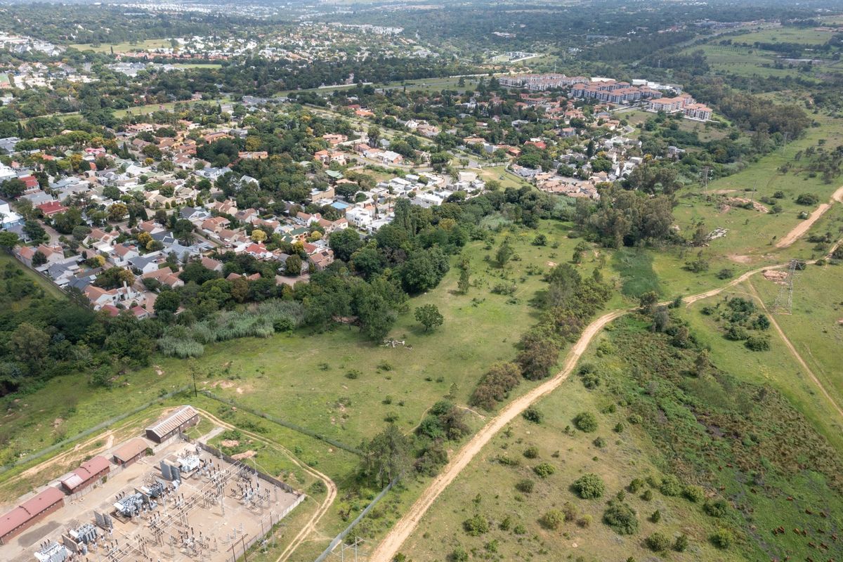 Aerial view of a large vacant residential plot adjacent to an established suburban neighborhood and an electrical substation.