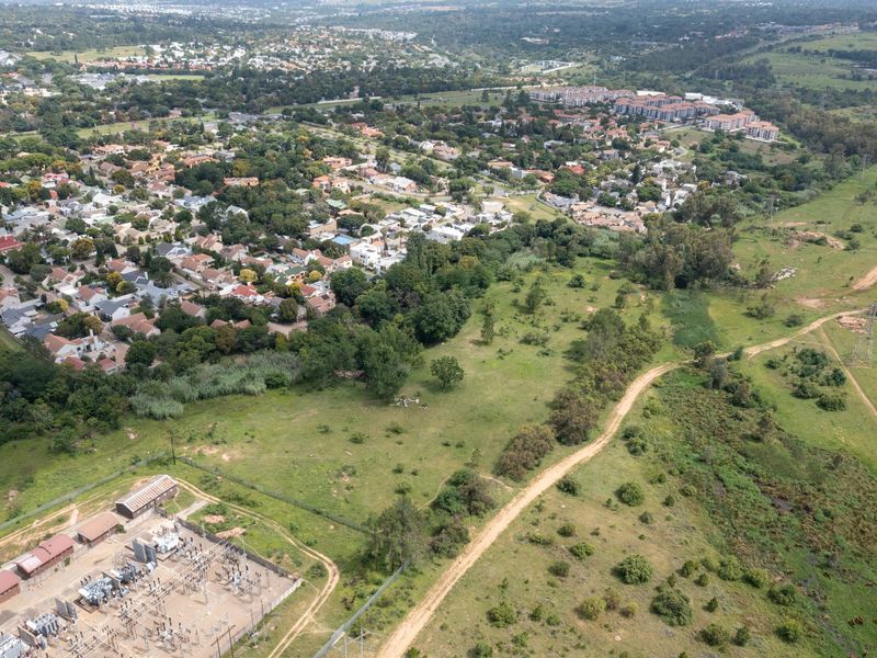 Aerial view of a large vacant residential plot adjacent to an established suburban neighborhood and an electrical substation.