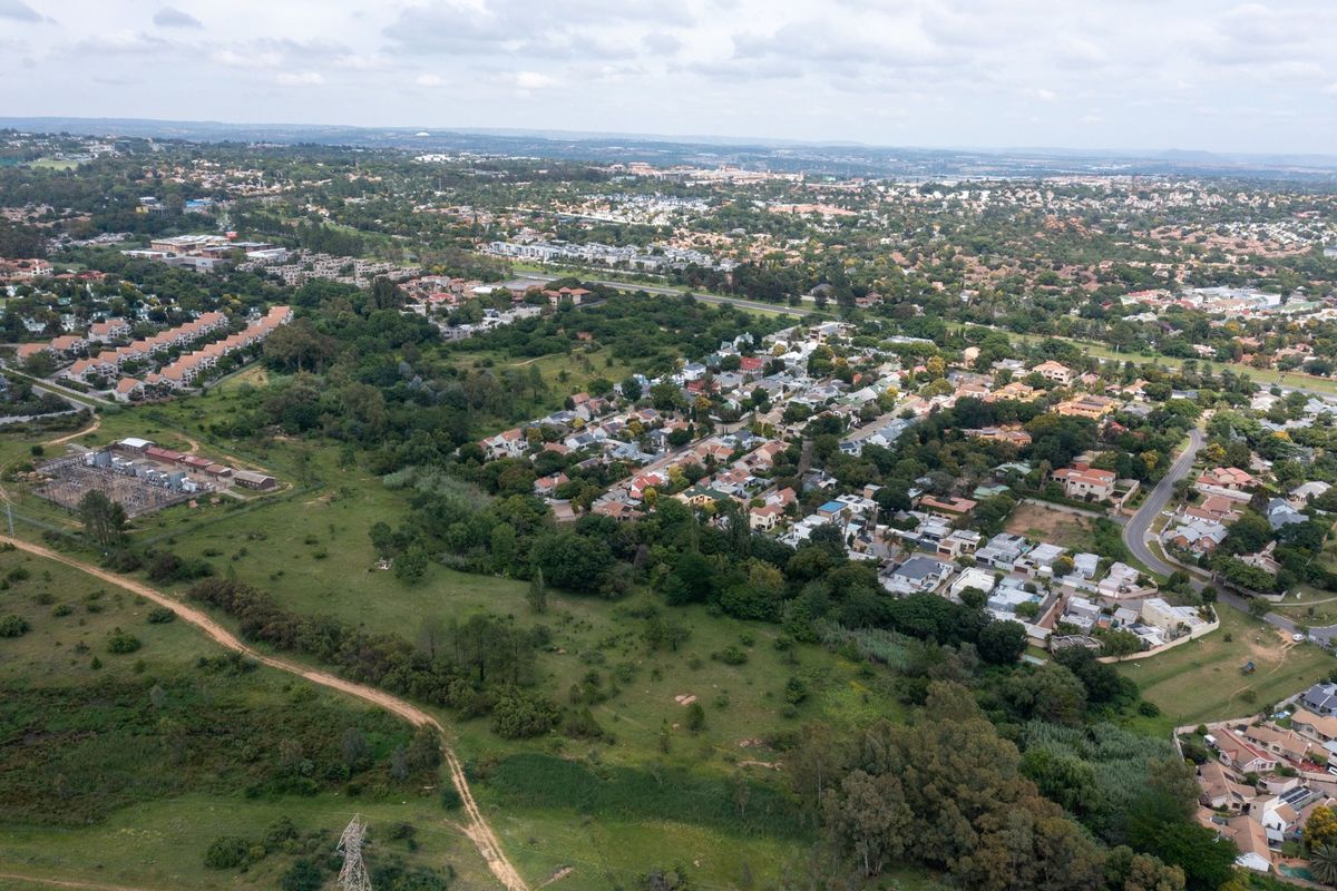 An aerial view of a vacant residential plot situated within an established suburban neighborhood, featuring surrounding greenery and nearby infrastructure.