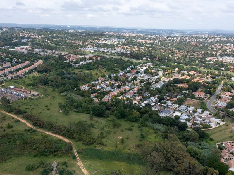 An aerial view of a vacant residential plot situated within an established suburban neighborhood, featuring surrounding greenery and nearby infrastructure.