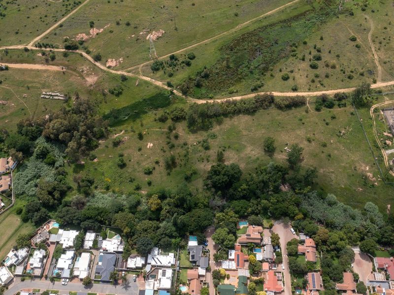 An aerial view of a large, undeveloped residential land parcel featuring natural vegetation and dirt access tracks, adjacent to an established residential neighborhood.