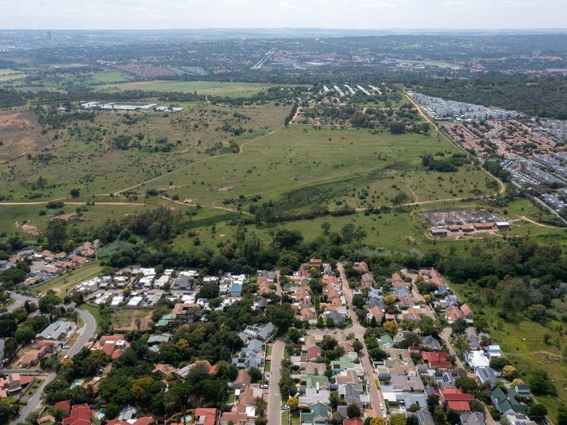 An aerial view showing a large expanse of undeveloped residential land adjacent to an established suburban neighborhood and an electrical substation.