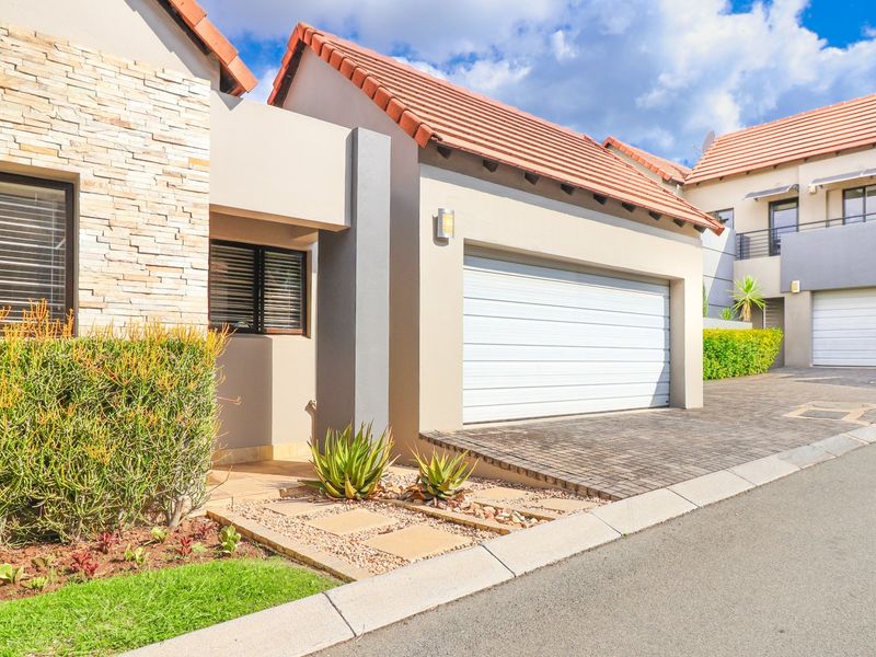 Modern front facade featuring stone cladding, a tiled roof, and a double garage with a paved driveway in a well-maintained residential setting.