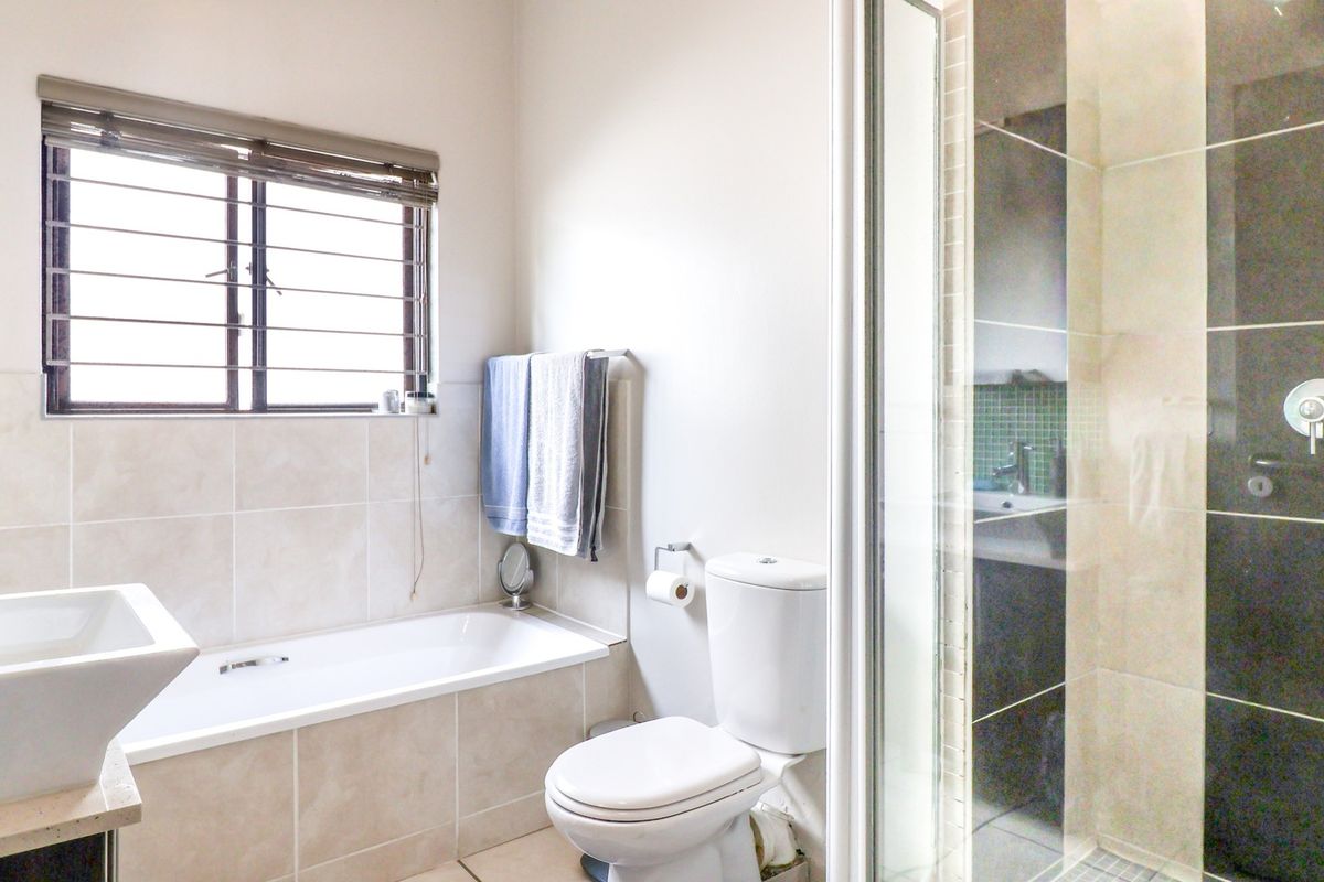 A functional bathroom featuring a built-in bathtub, separate shower enclosure, toilet, and vanity basin with neutral wall and floor tiling.