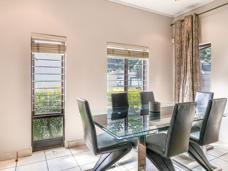 A bright dining room featuring tiled flooring and large windows with security bars, providing natural light and a view of the exterior.