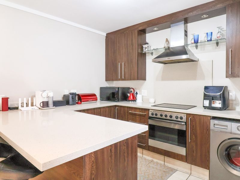 Modern kitchen featuring dark wood cabinetry, stone countertops, a breakfast bar, and integrated appliances including an oven, hob, and washing machine.