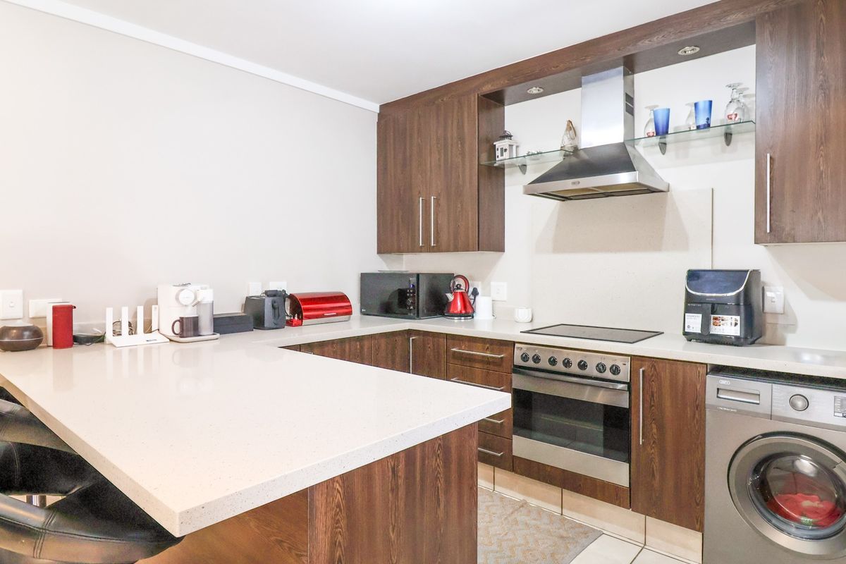 Modern kitchen featuring dark wood cabinetry, stone countertops, a breakfast bar, and integrated appliances including an oven, hob, and washing machine.