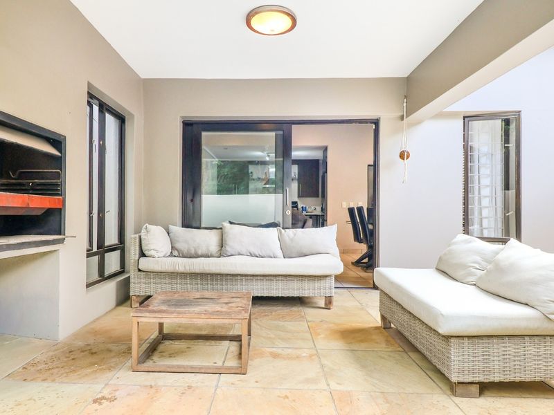 Covered patio area featuring stone tile flooring and a built-in braai, providing a seamless transition to the interior living space through sliding glass doors.