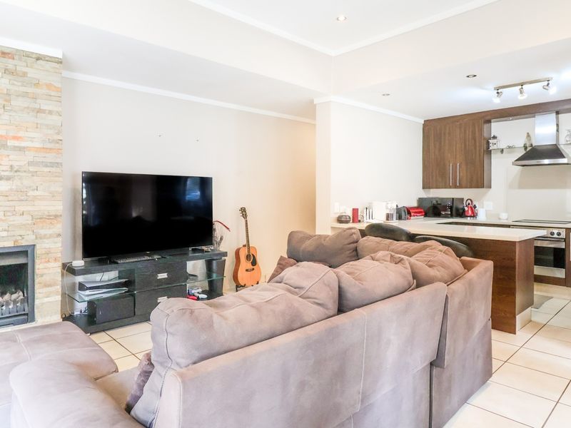 Open-plan living area featuring a stone-clad fireplace and a modern kitchen with built-in cabinetry, integrated appliances, and tiled flooring throughout.