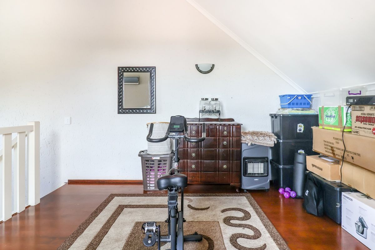 An attic-style living space featuring sloped ceilings, wooden flooring, and a staircase railing, currently utilized as a multi-purpose storage and exercise area.