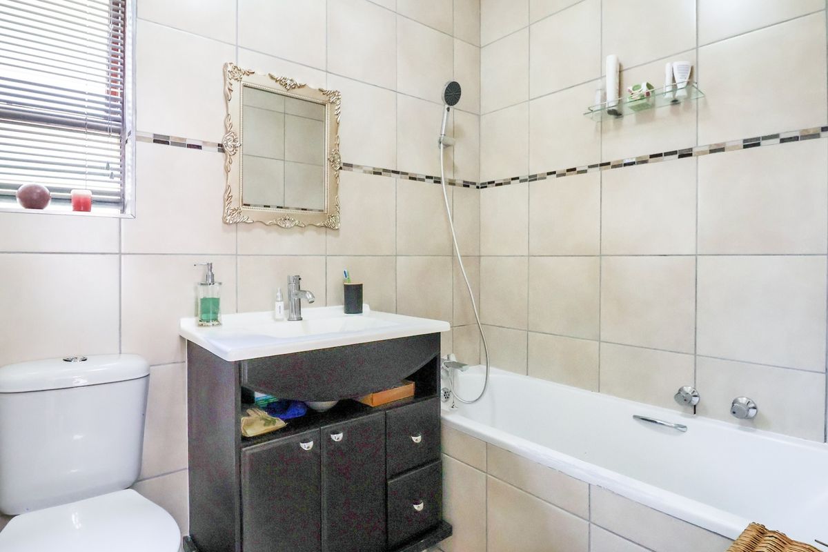 A functional bathroom featuring a vanity cabinet with basin, a bathtub with shower attachment, and a toilet, finished with neutral wall tiling.