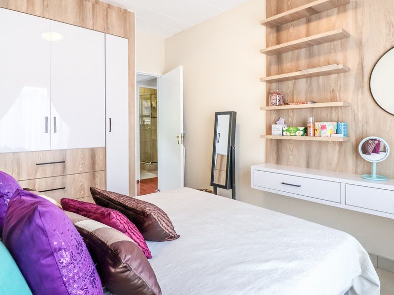 A well-maintained bedroom featuring modern wood-grain built-in wardrobes, a floating vanity with integrated shelving, and neutral finishes.