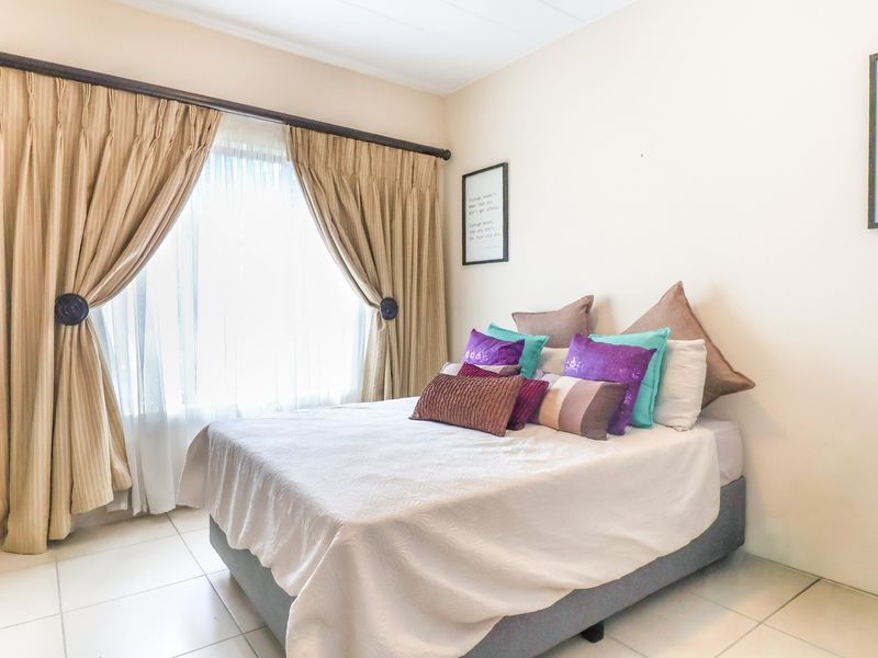 A well-lit bedroom featuring tiled flooring, neutral walls, and a large window with installed curtain rods and built-in shelving.