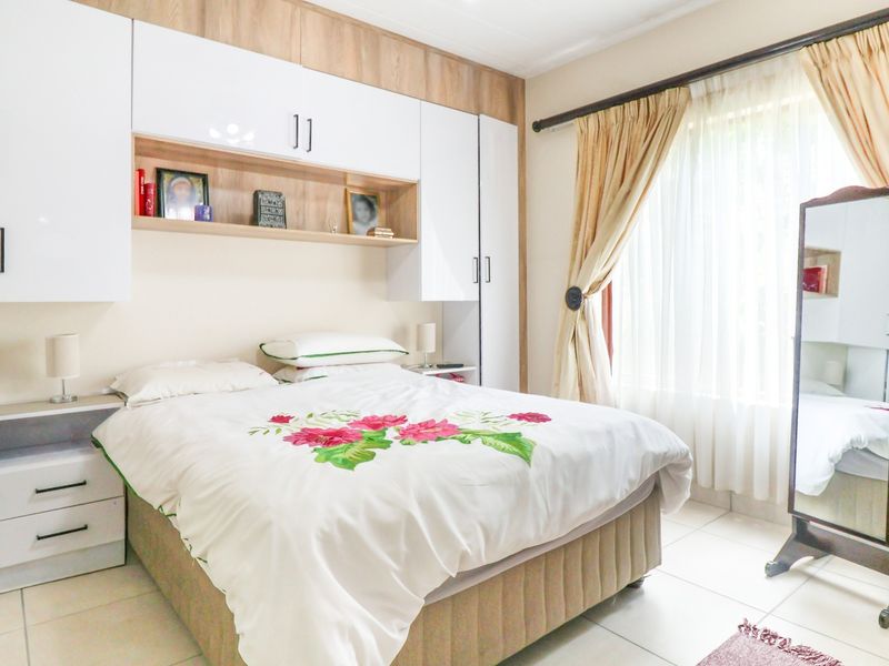 A well-maintained bedroom featuring extensive built-in cabinetry, neutral tiled flooring, and large windows with curtain rails for natural light.