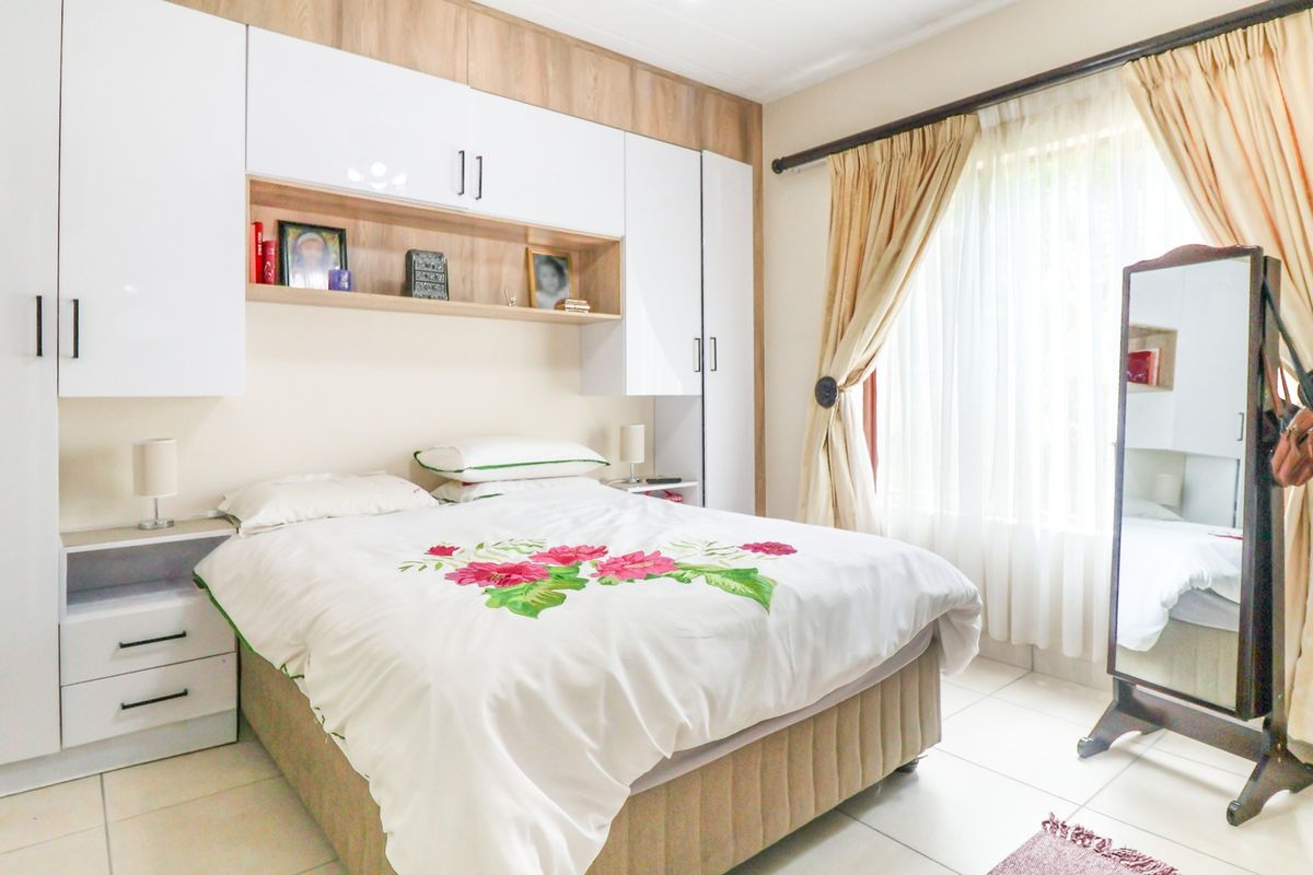 A well-maintained bedroom featuring extensive built-in cabinetry, neutral tiled flooring, and large windows with curtain rails for natural light.
