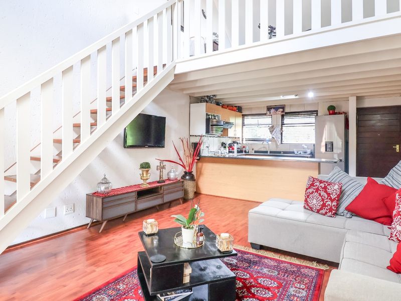 Open plan living area featuring a staircase leading to a mezzanine level, integrated kitchen with cabinetry, and warm wooden flooring throughout.