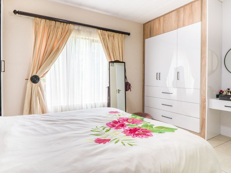 A well-maintained bedroom featuring modern built-in cupboards with a matching integrated vanity unit and neutral tiled flooring.