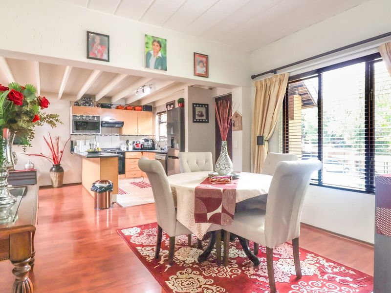 Open-plan living and dining area featuring laminate flooring, exposed ceiling beams, and a functional kitchen with built-in cabinetry and integrated appliances.