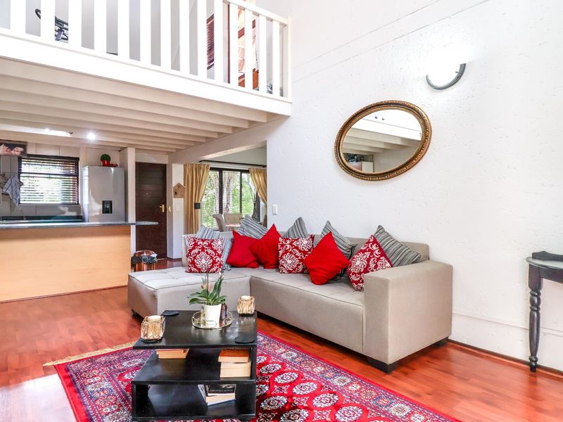 Open-plan living area featuring laminate flooring, exposed ceiling beams, and a mezzanine level with a timber balustrade, overlooking a functional kitchen space.