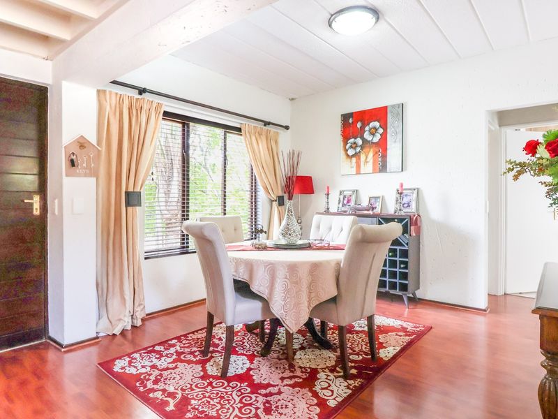 Dining area featuring laminate flooring, exposed beam ceiling, and natural light through a window with venetian blinds.