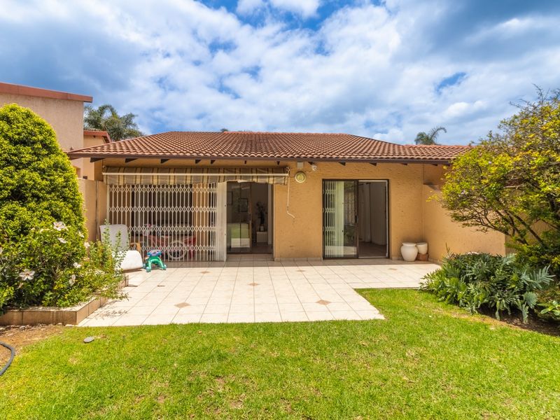 Rear view of the townhouse featuring a paved patio area, retractable awning, security gates, and access to the garden.
