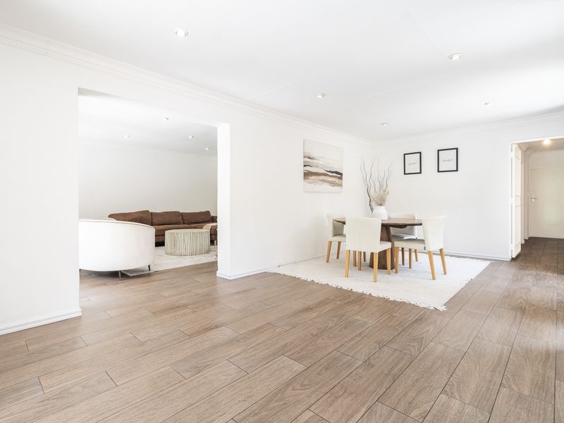 Spacious open-plan living and dining area featuring modern wood-look tile flooring, recessed downlights, and clean white finishes throughout.
