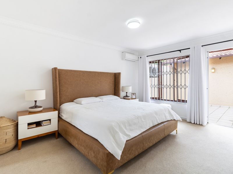 Spacious bedroom featuring carpeted flooring, air conditioning, and direct access to an outdoor patio area through a sliding door with security gate.
