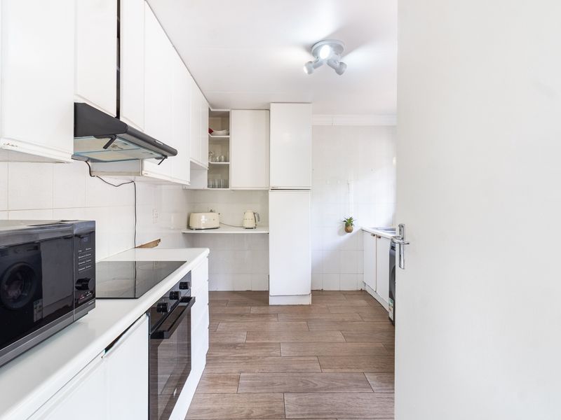 A functional kitchen featuring white cabinetry, a built-in oven, electric hob, extractor fan, and tiled flooring with a clean, neutral aesthetic.