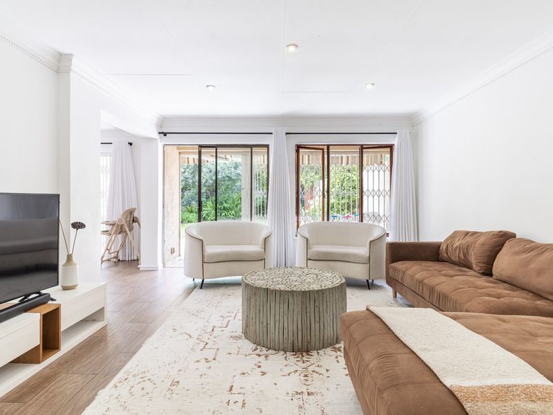 Bright and spacious living room featuring laminate flooring, crown molding, recessed lighting, and large sliding glass doors providing access to the garden.