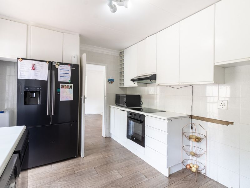 Functional kitchen featuring white cabinetry, built-in oven and hob, extractor fan, and tiled backsplash, with wood-look laminate flooring throughout.
