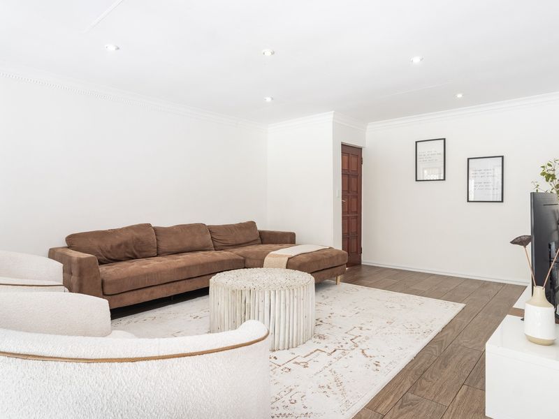 A bright and spacious living room featuring timber-look flooring, recessed downlighting, and decorative ceiling cornices, creating a clean and inviting atmosphere.