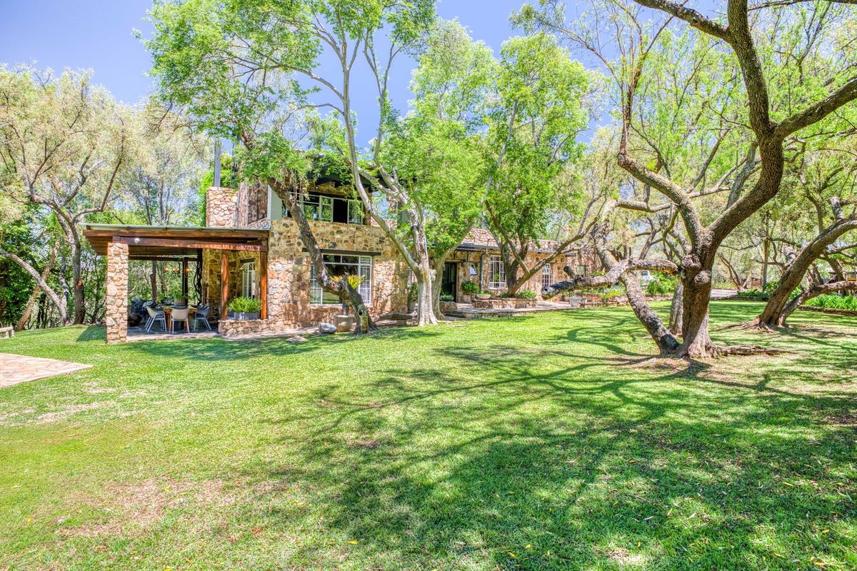 A charming stone-clad residence featuring a spacious covered patio and a lush, mature garden setting.