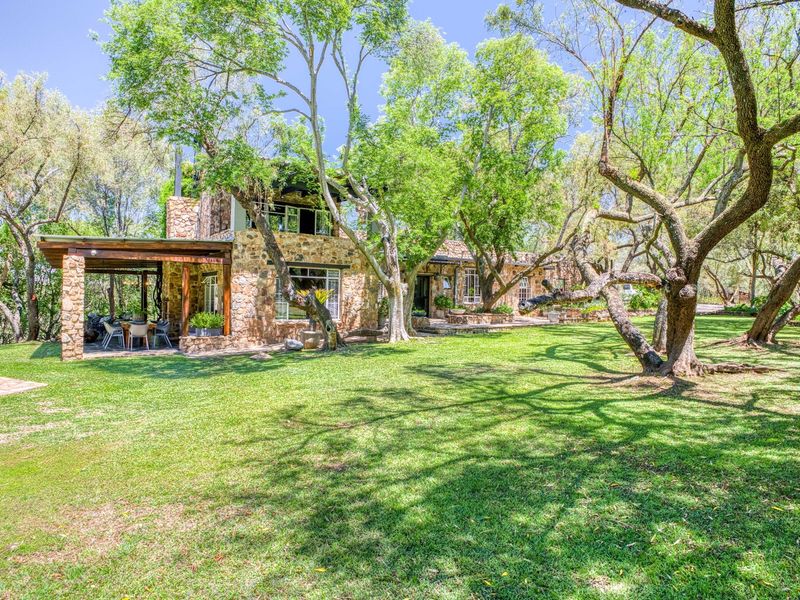 A charming stone-clad residence featuring a spacious covered patio and a lush, mature garden setting.