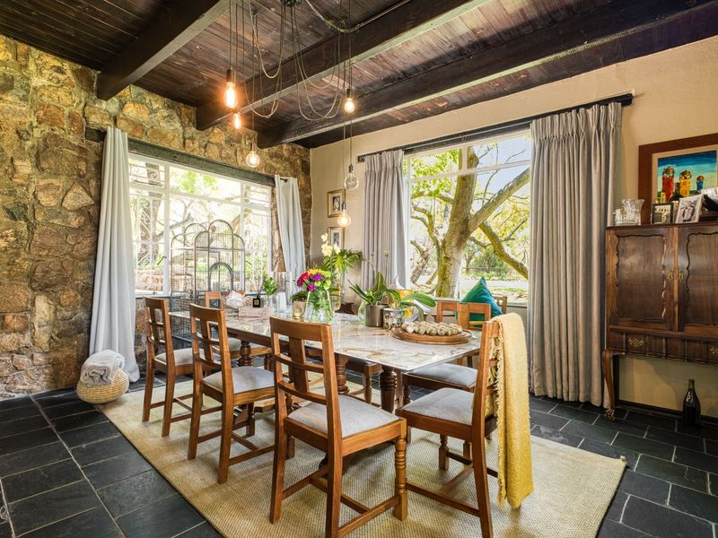 A charming dining room featuring a rustic stone feature wall, exposed timber ceiling beams, and slate tile flooring with large windows overlooking the garden.