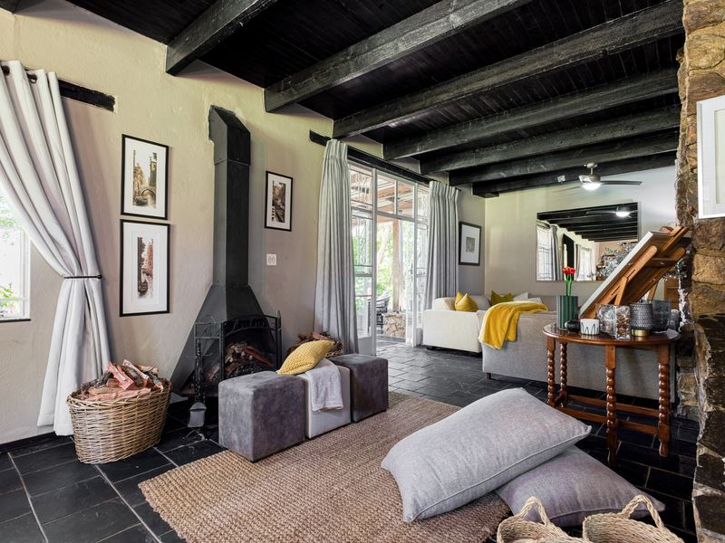 Cozy living room featuring exposed dark timber ceiling beams, a striking stone feature wall, a freestanding metal fireplace, and durable slate tile flooring.