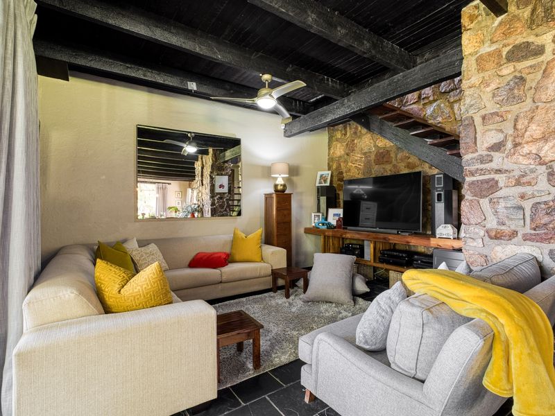 Cozy living room featuring a rustic stone feature wall, exposed dark timber ceiling beams, and slate tile flooring.