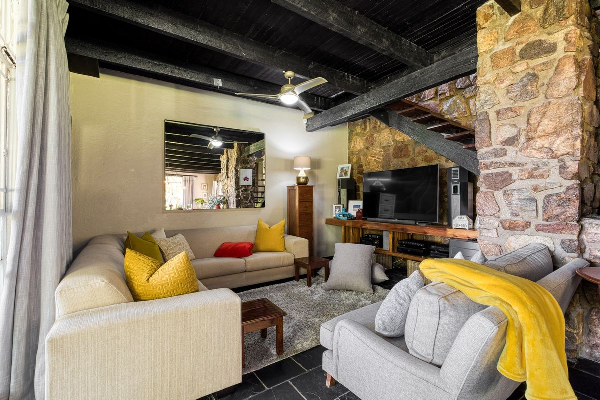 Cozy living room featuring a rustic stone feature wall, exposed dark timber ceiling beams, and slate tile flooring.