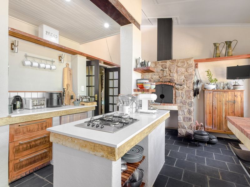 Spacious kitchen featuring a rustic stone fireplace, central island with gas hob, stone countertops, and slate flooring, blending traditional charm with modern functionality.