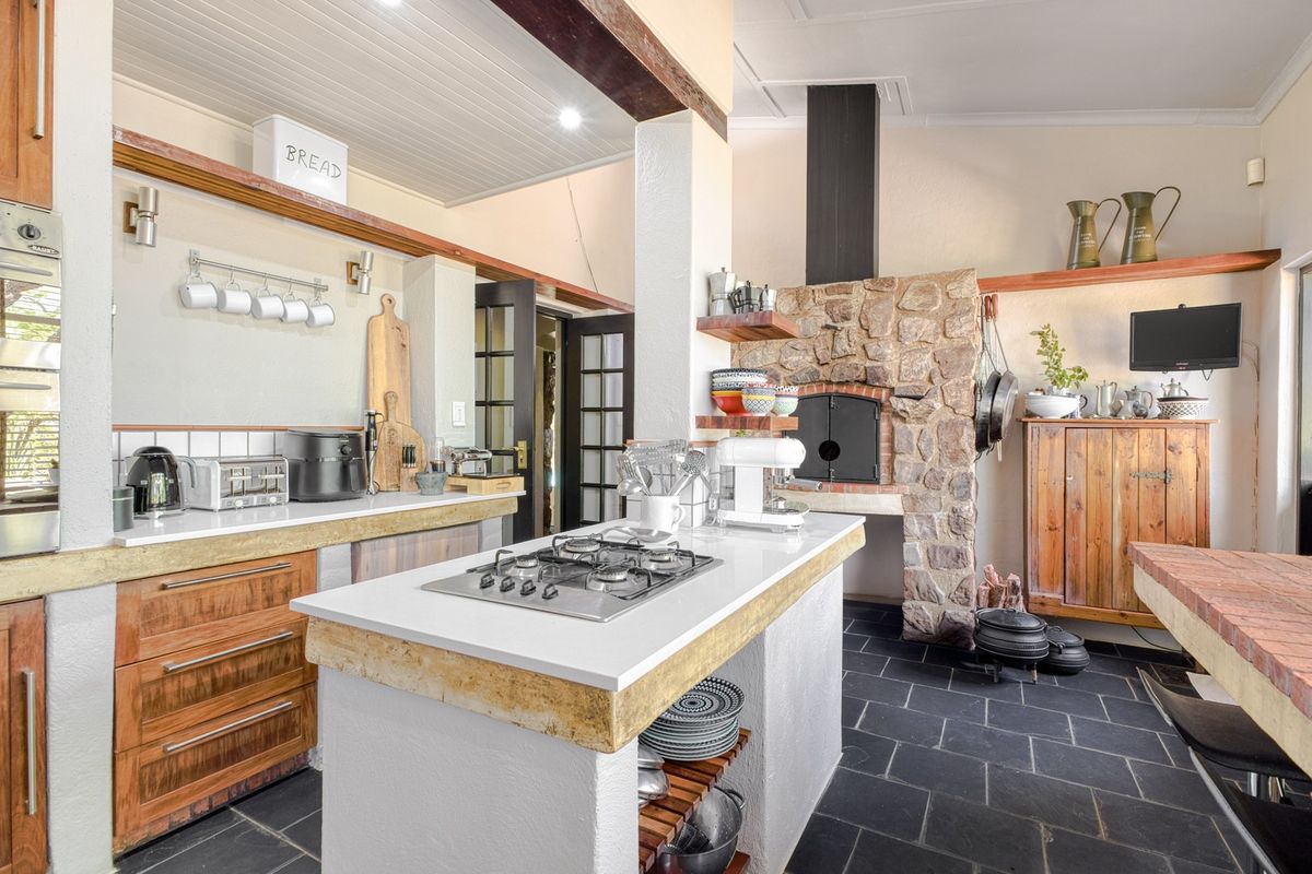 Spacious kitchen featuring a rustic stone fireplace, central island with gas hob, stone countertops, and slate flooring, blending traditional charm with modern functionality.