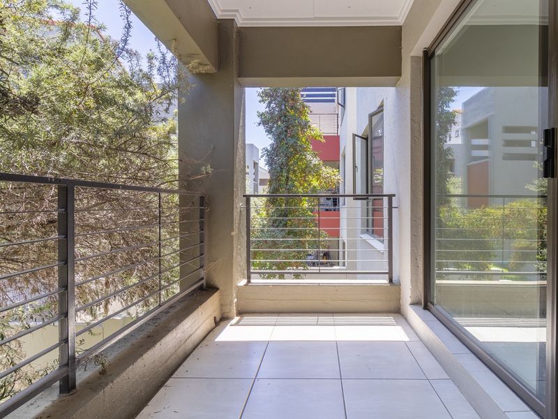 A covered balcony featuring tiled flooring and a metal balustrade, providing an outdoor extension to the apartment living space.